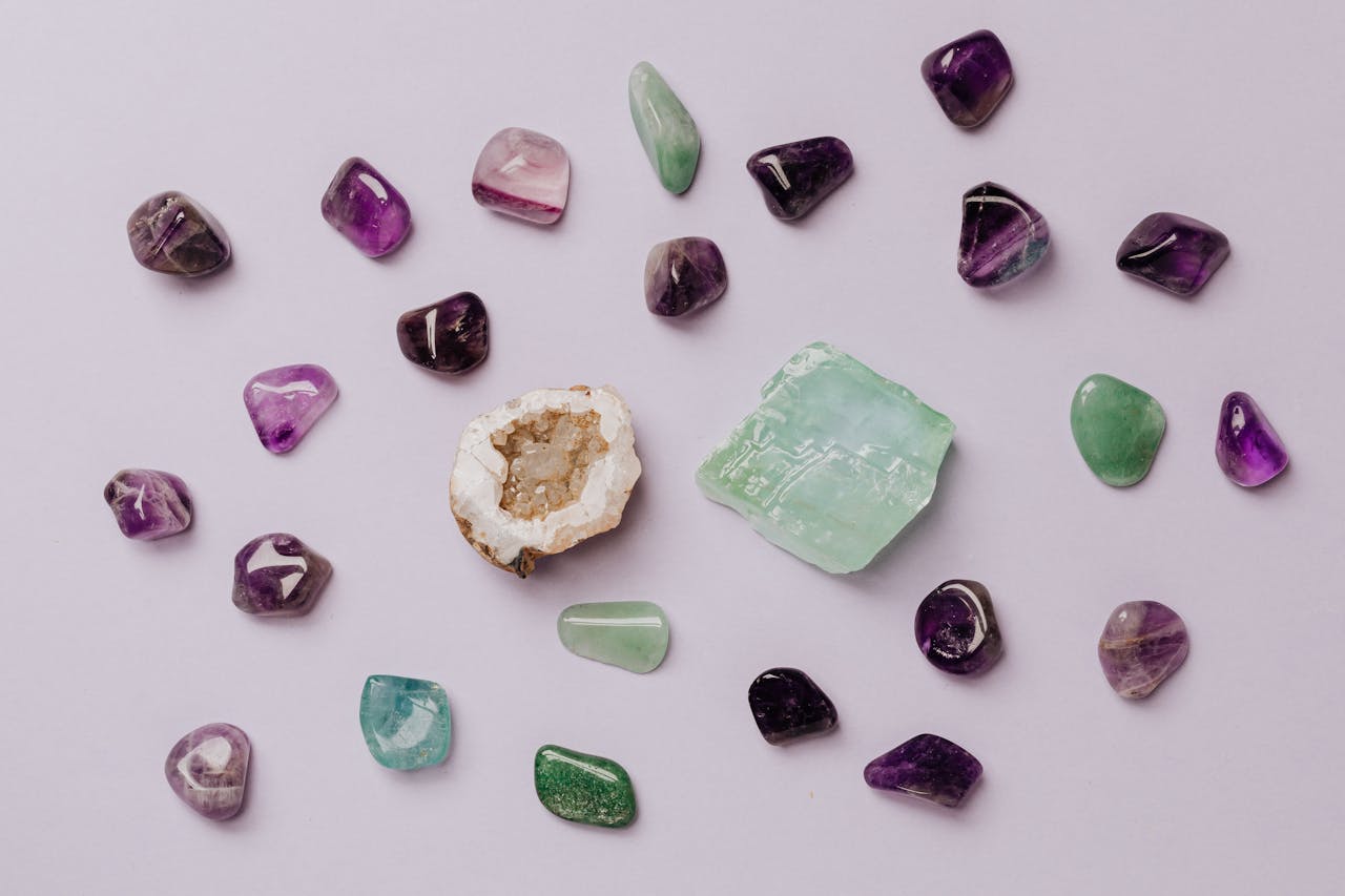 about-us Flat lay of assorted polished gemstones including amethyst and jade on a light background.